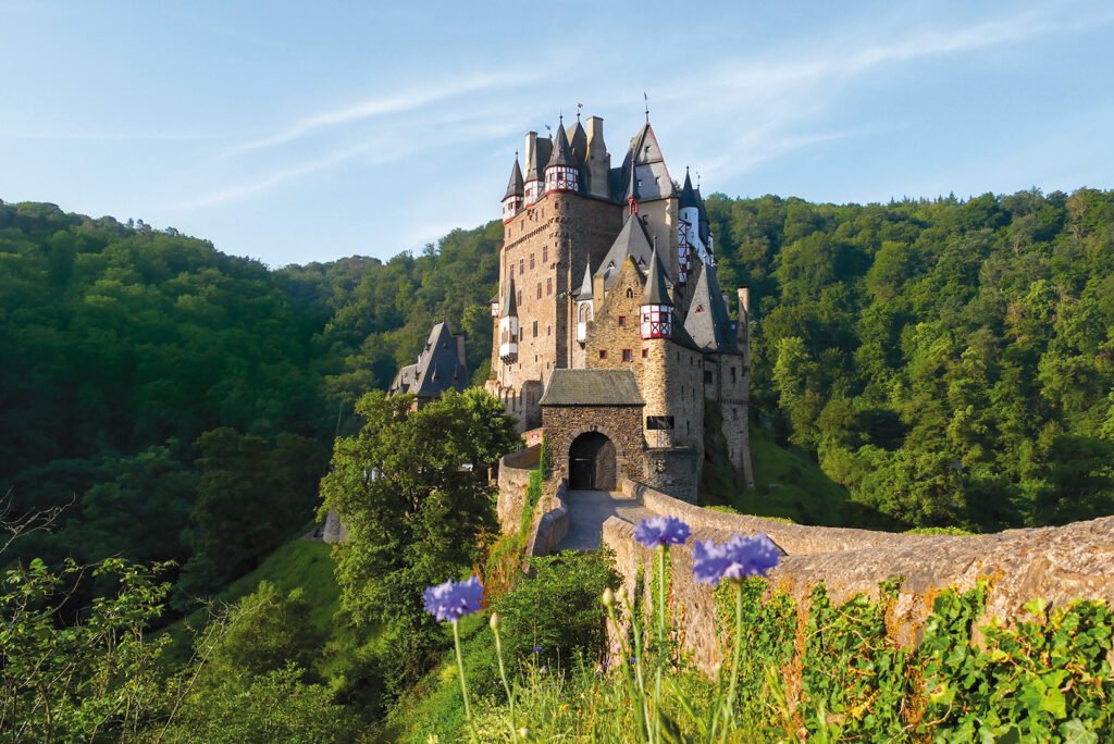 Eltz Castle on a sunny day with flowers on the path to its entrance.