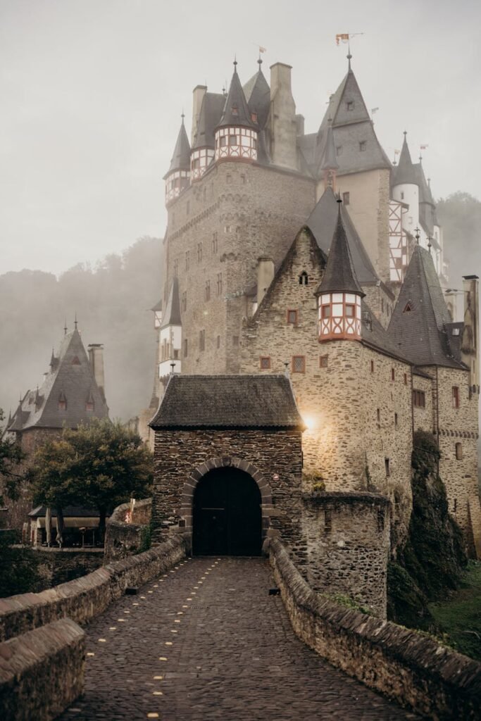 Eltz Castle under cloudy skies. A brown stone castle with pointed half-timbered towers. 